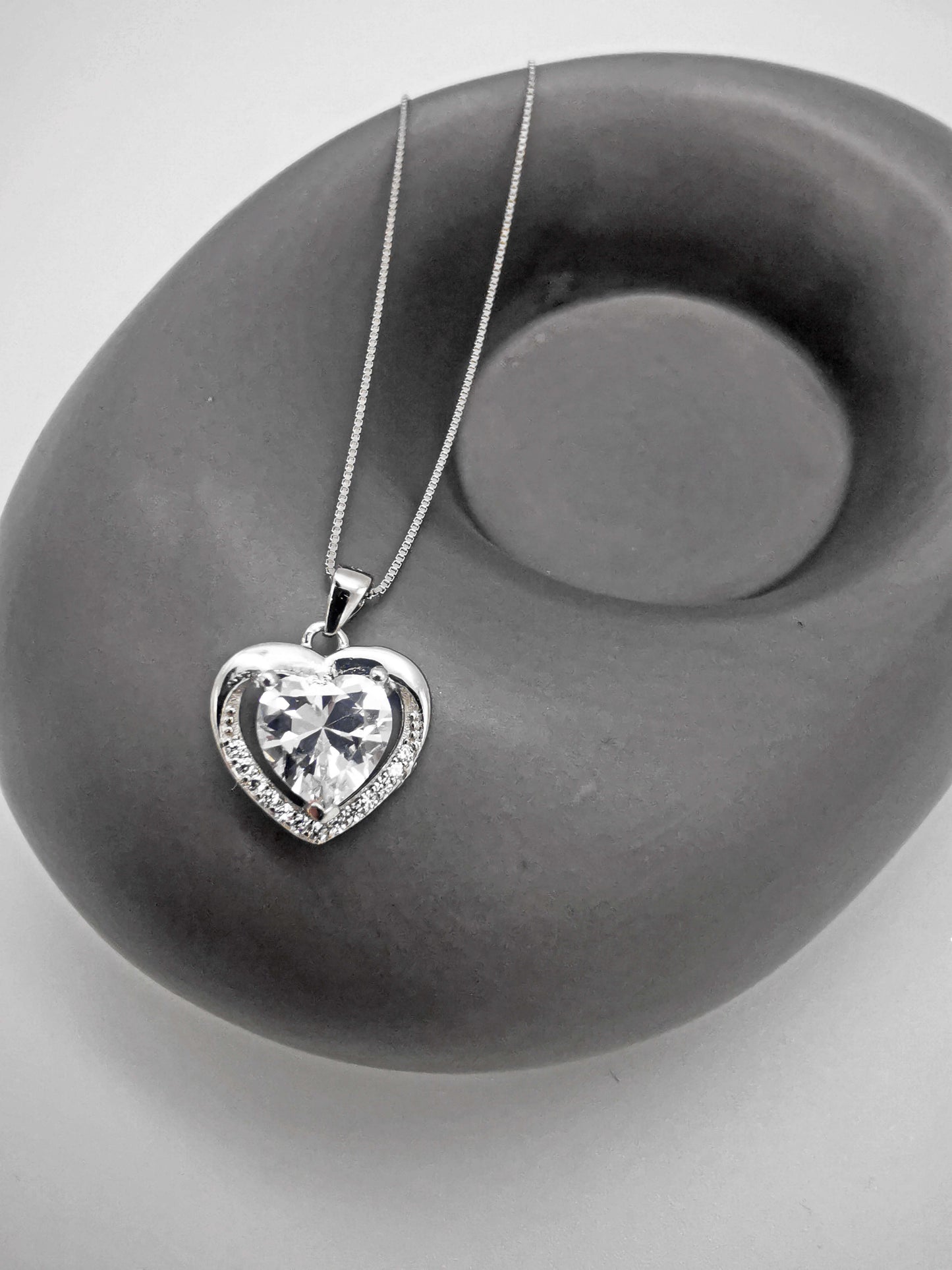 Sterling silver heart necklace with sparkling centre stone and pavé border, displayed on a modern grey stone prop. Elegant and timeless gift for her—ideal for Valentine’s Day, anniversary, or romantic occasions