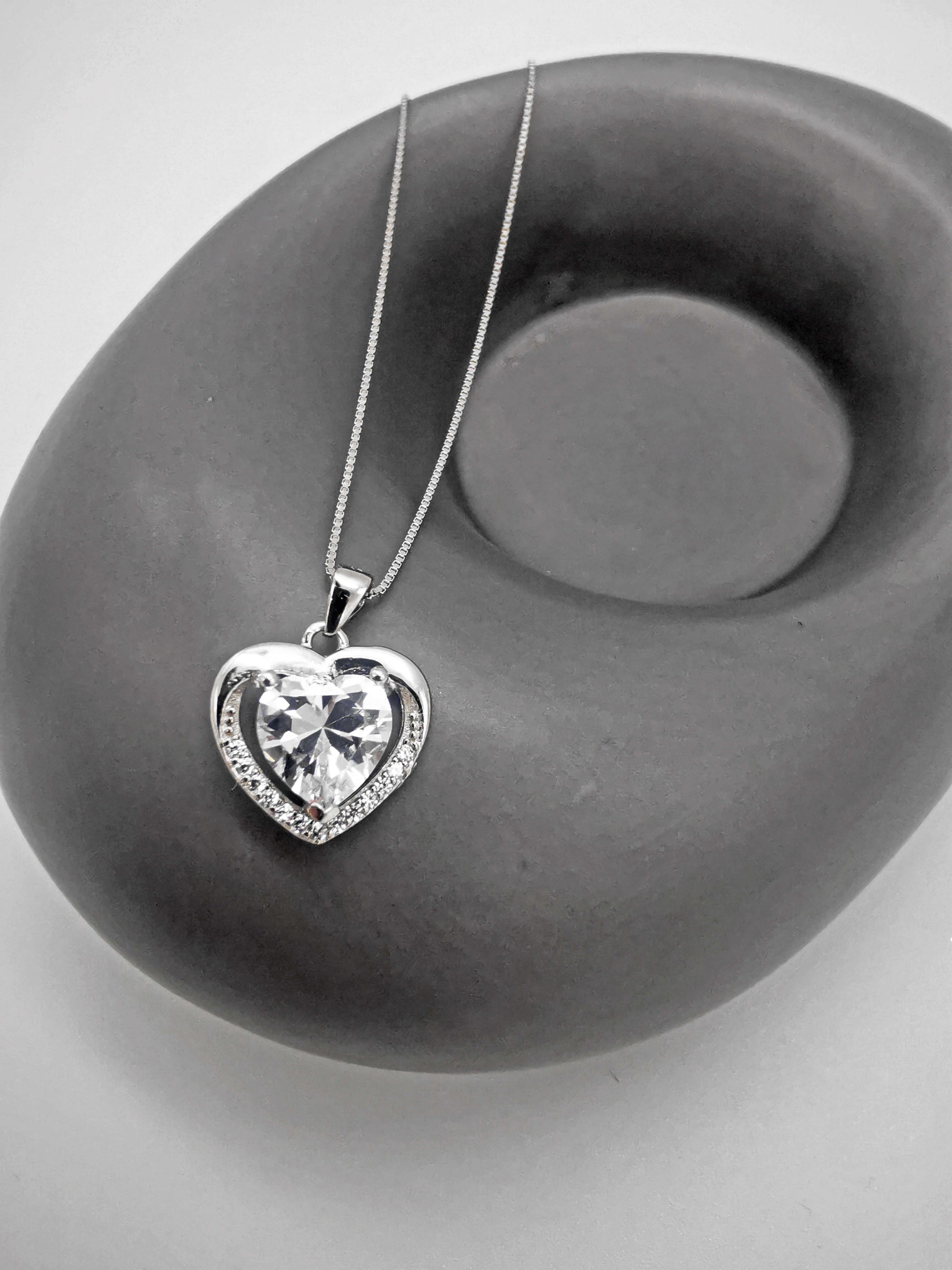 Sterling silver heart necklace with sparkling centre stone and pavé border, displayed on a modern grey stone prop. Elegant and timeless gift for her—ideal for Valentine’s Day, anniversary, or romantic occasions