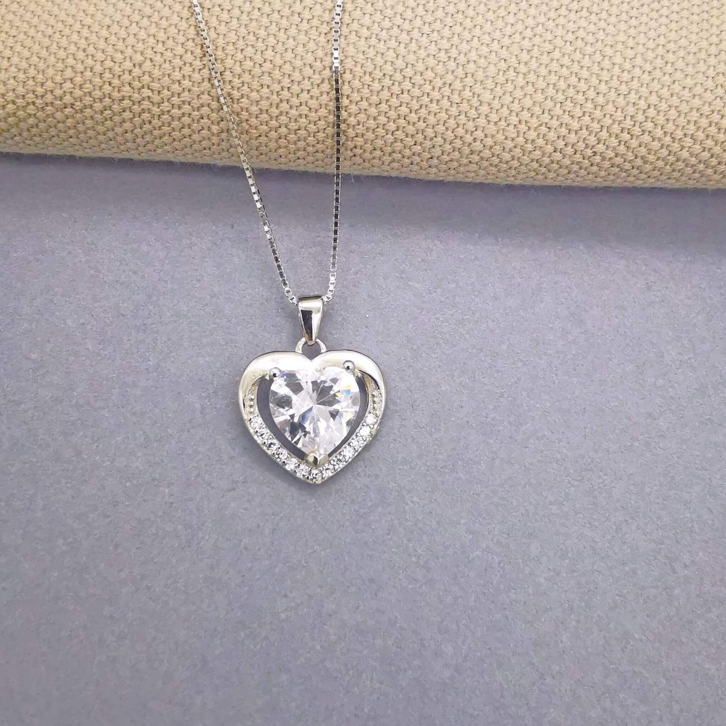 Elegant sterling silver heart pendant necklace with a brilliant centre stone and pavé crystal border, styled on a neutral fabric and grey background. Romantic jewellery gift for her—perfect for Valentine’s Day, anniversary, or birthday.