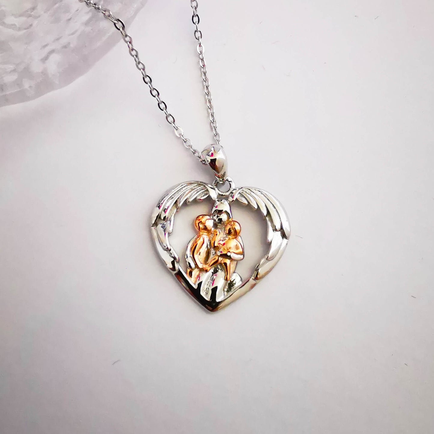 Sterling silver and rose gold pendant necklace. Depicts mum hugging two children under wings. Gift for mum.