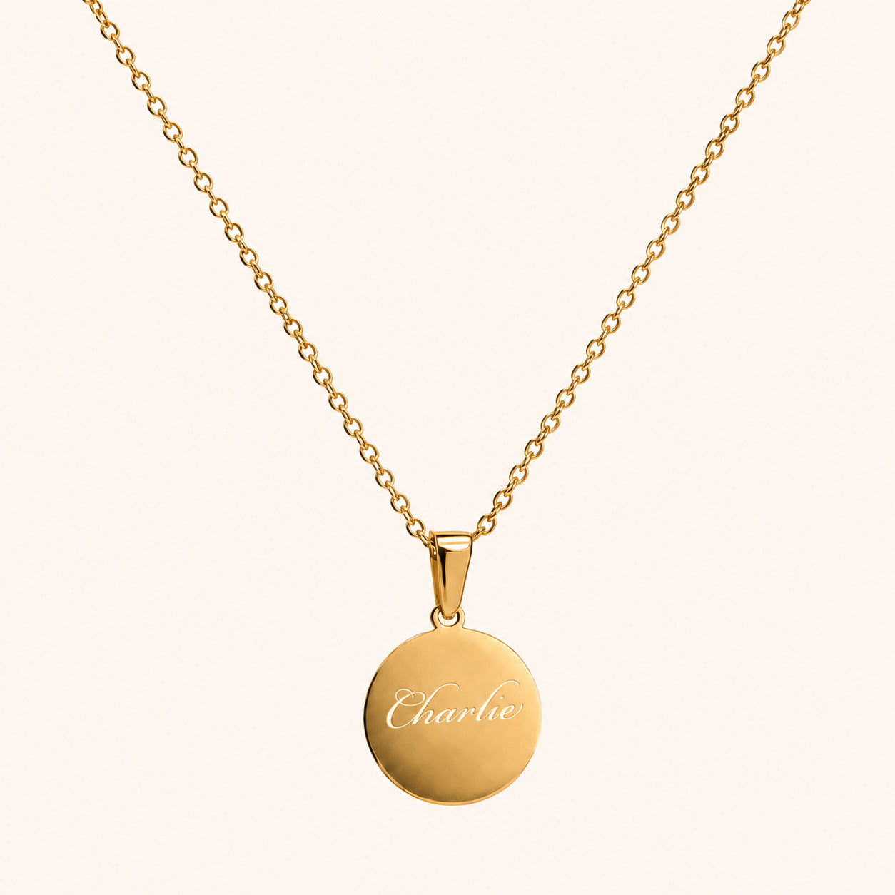 Gold necklace with a round pendant engraved with 'Charlie' on a white background