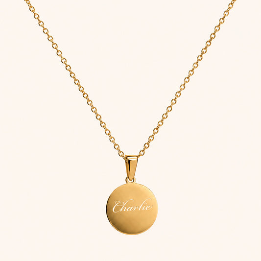 Gold necklace with a round pendant engraved with 'Charlie' on a white background