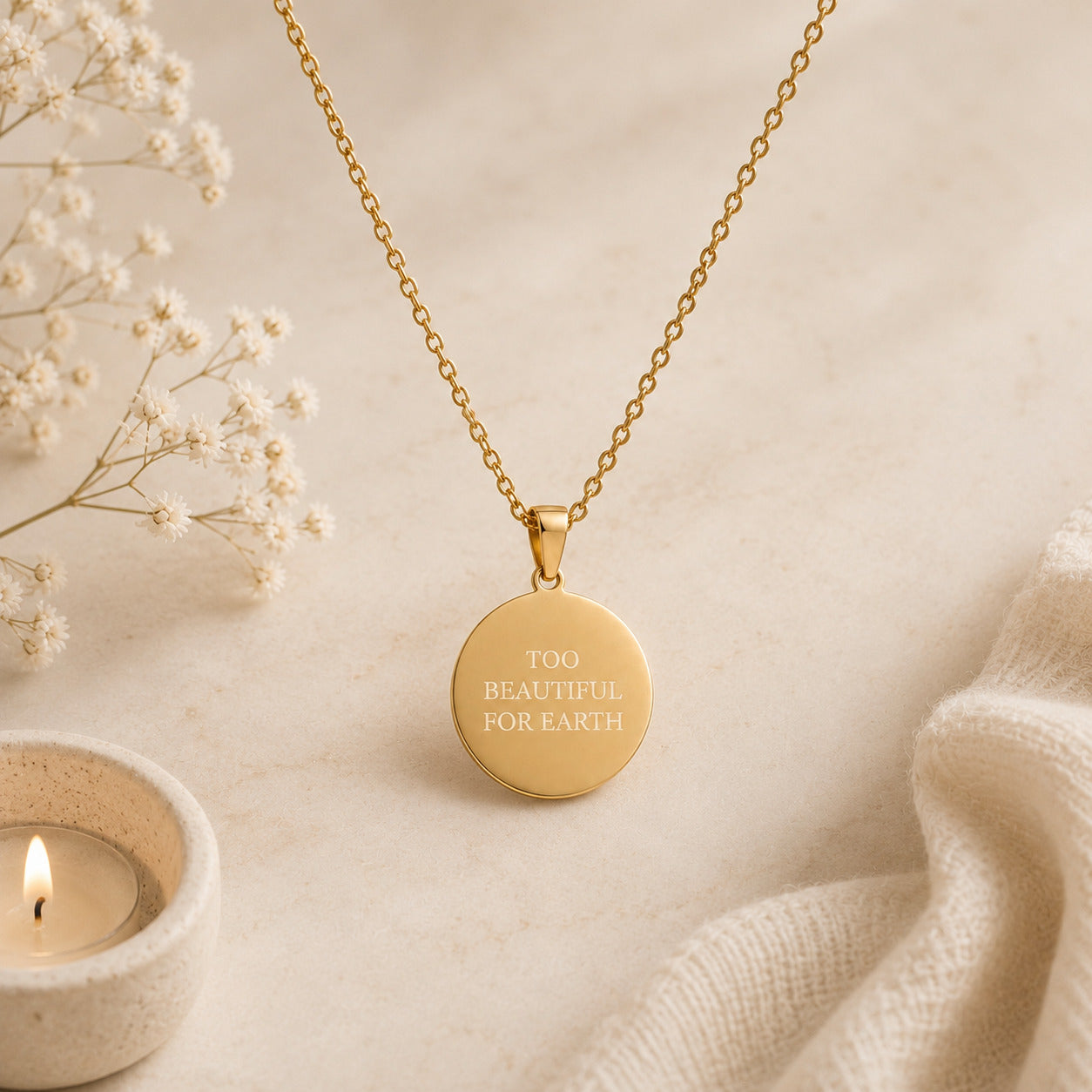 Gold necklace with 'TOO BEAUTIFUL FOR EARTH' pendant on a soft beige background with flowers and a candle.